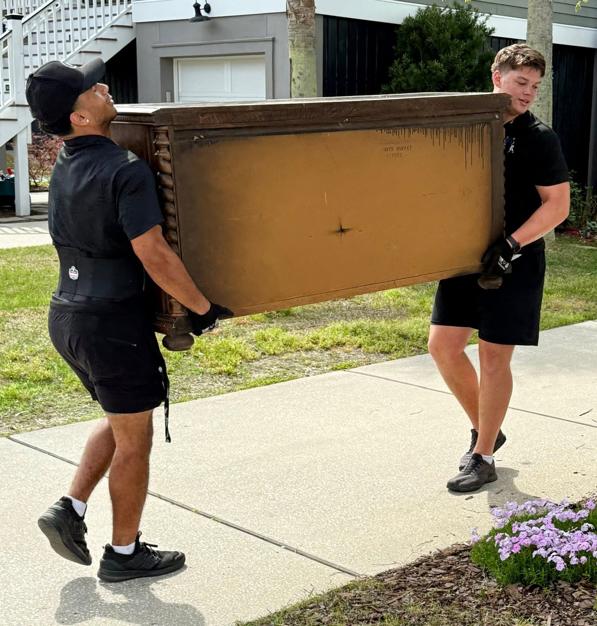 Two Arnold Brothers movers carrying a wooden dresser