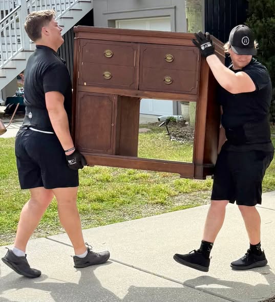Two Arnold Brothers movers carrying a wooden dresser